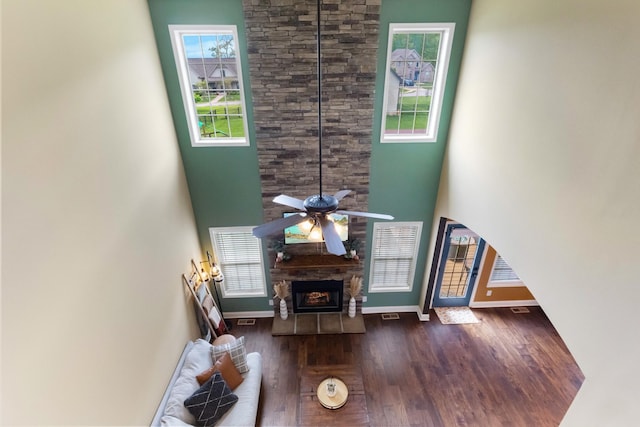 living room featuring a ceiling fan, a towering ceiling, a fireplace, wood finished floors, and baseboards