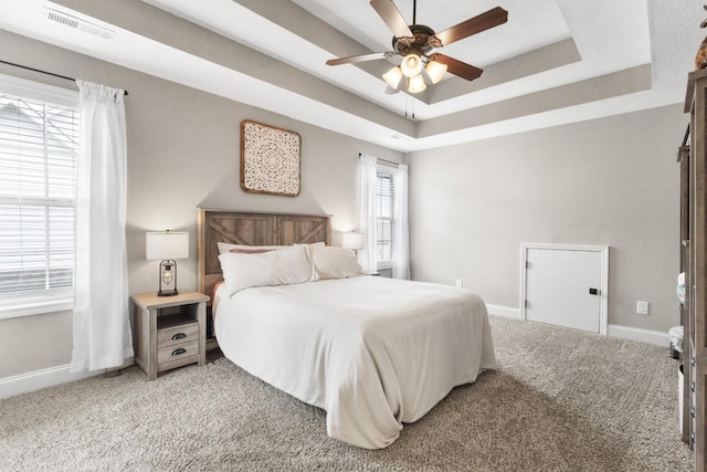 bedroom with visible vents, light carpet, baseboards, a tray ceiling, and a ceiling fan