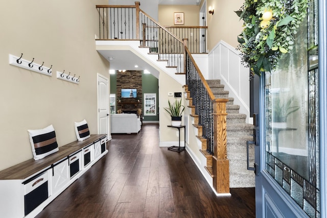 entrance foyer with a towering ceiling, a fireplace, baseboards, dark wood-style floors, and stairs