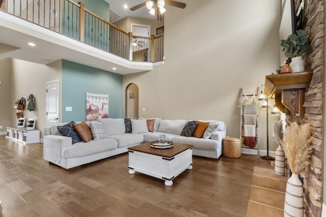 living room with arched walkways, a high ceiling, ceiling fan, and wood finished floors