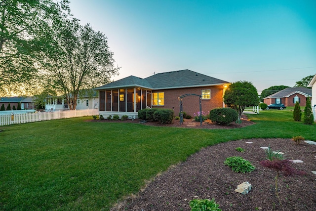 view of front of property featuring roof with shingles, a sunroom, brick siding, fence, and a front lawn