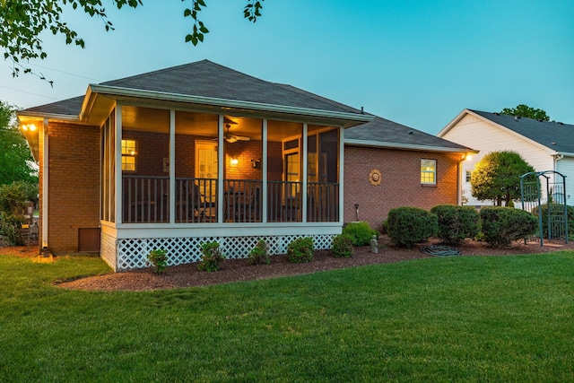 rear view of property with a lawn, a sunroom, roof with shingles, and brick siding