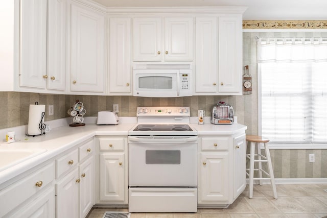 kitchen featuring light countertops, white cabinets, a healthy amount of sunlight, and white appliances