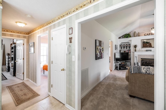 corridor with a textured ceiling, light colored carpet, visible vents, baseboards, and lofted ceiling