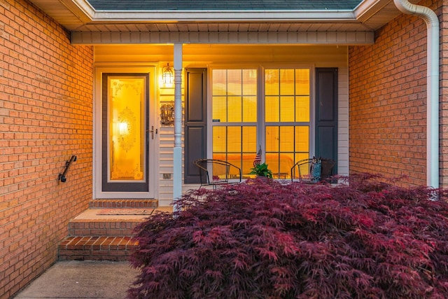 entrance to property featuring covered porch, brick siding, and roof with shingles