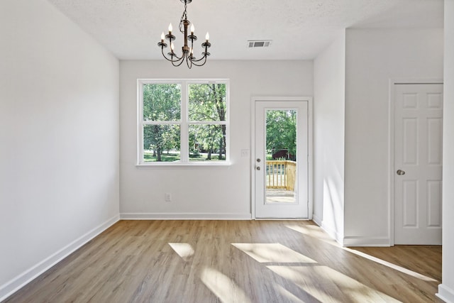 unfurnished dining area featuring a notable chandelier, visible vents, light wood-style flooring, baseboards, and a textured ceiling