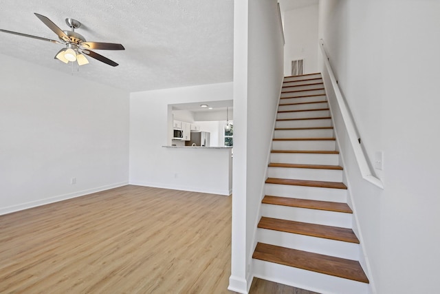 stairway with wood finished floors, ceiling fan, baseboards, visible vents, and a textured ceiling