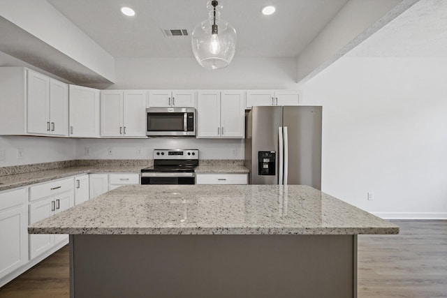 kitchen featuring light stone counters, white cabinets, stainless steel appliances, a kitchen island, and wood finished floors