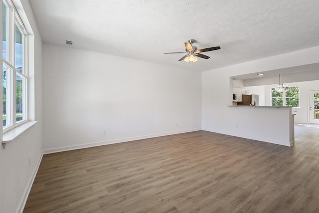 unfurnished living room featuring visible vents, baseboards, a textured ceiling, wood finished floors, and ceiling fan with notable chandelier