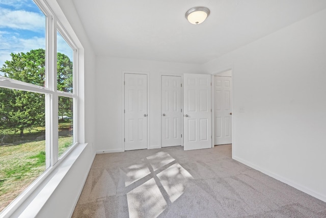 unfurnished bedroom featuring baseboards, carpet, multiple windows, and two closets