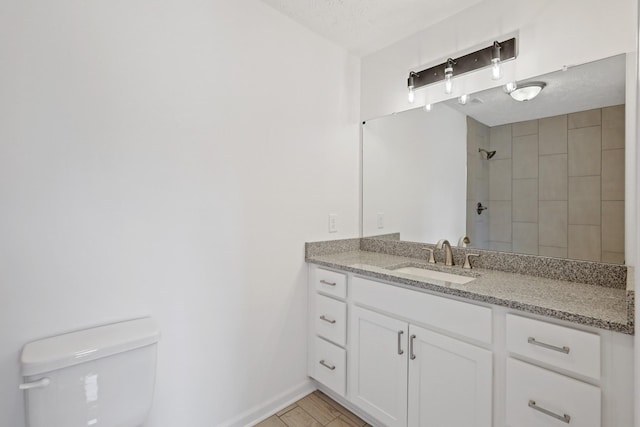 full bath featuring vanity, toilet, tiled shower, and baseboards