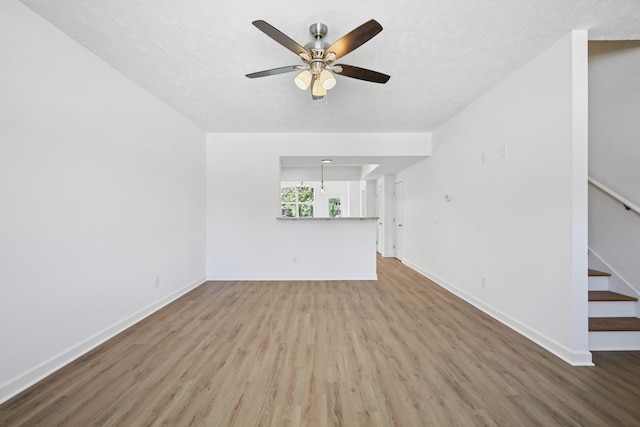 unfurnished living room with stairs, ceiling fan, wood finished floors, and baseboards