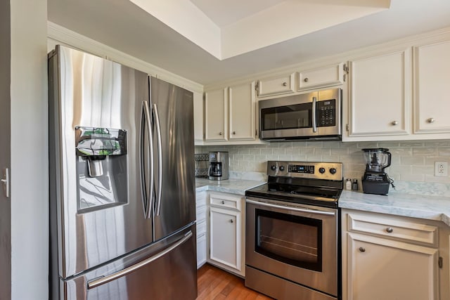 kitchen featuring white cabinets, wood finished floors, appliances with stainless steel finishes, and decorative backsplash