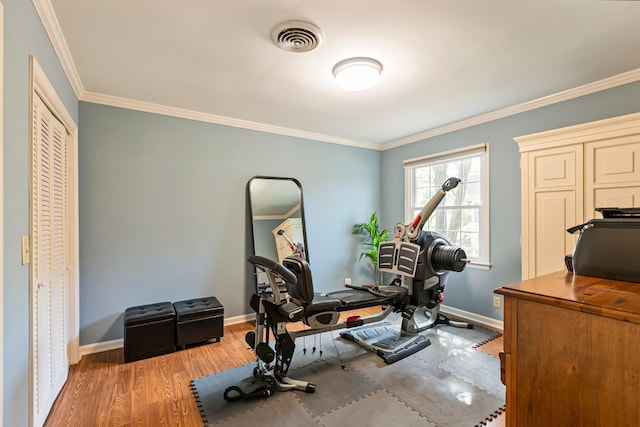 exercise room with wood finished floors, visible vents, ornamental molding, and baseboards