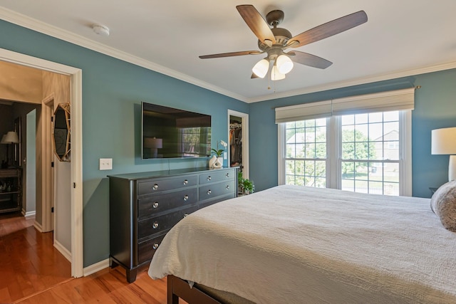 bedroom with ceiling fan, baseboards, ornamental molding, wood finished floors, and a walk in closet