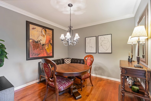 dining space with baseboards, wood finished floors, a notable chandelier, and ornamental molding