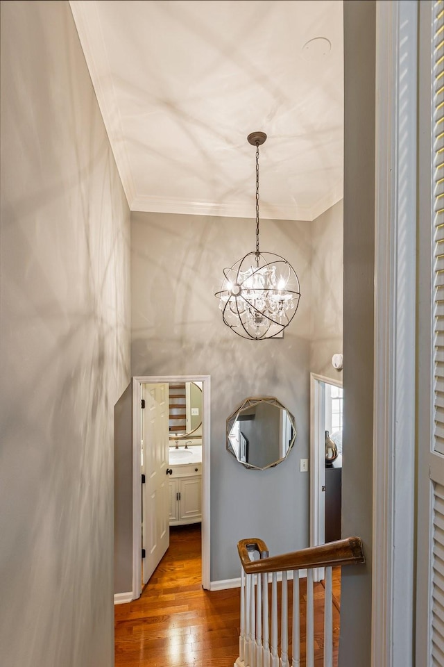 corridor featuring a chandelier, wood finished floors, a high ceiling, and crown molding