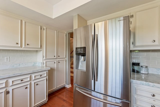 kitchen featuring light stone countertops, backsplash, stainless steel fridge, and dark wood finished floors