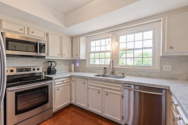 kitchen featuring light stone counters, decorative backsplash, stainless steel appliances, a sink, and dark wood-type flooring