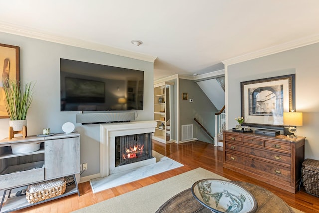 living area featuring wood finished floors, visible vents, crown molding, and stairway