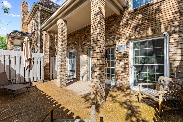 exterior space featuring a chimney, brick siding, fence, and a patio