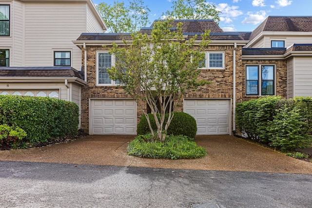 townhome / multi-family property featuring driveway, brick siding, and a garage