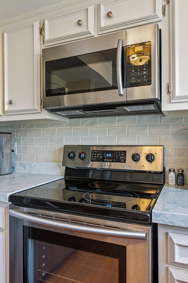 kitchen with white cabinets, light stone counters, stainless steel appliances, and decorative backsplash