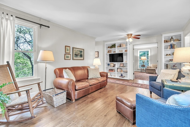 living room featuring wood finished floors, ceiling fan, built in features, and crown molding