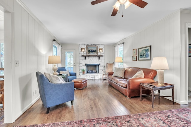 living room with ceiling fan, a stone fireplace, wood finished floors, and baseboards