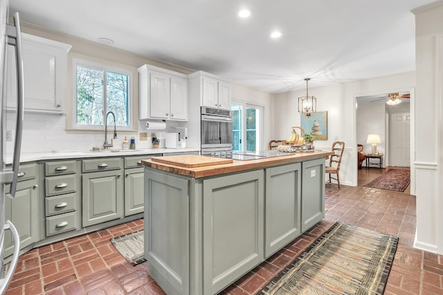 kitchen featuring green cabinetry, a sink, stainless steel appliances, butcher block counters, and brick floor