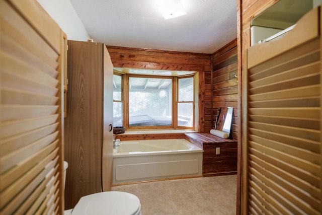 full bath featuring wood walls, toilet, a garden tub, and a textured ceiling
