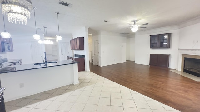 kitchen featuring a sink, a fireplace with flush hearth, visible vents, dark countertops, and ceiling fan with notable chandelier
