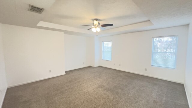 empty room featuring dark carpet, a raised ceiling, visible vents, and baseboards