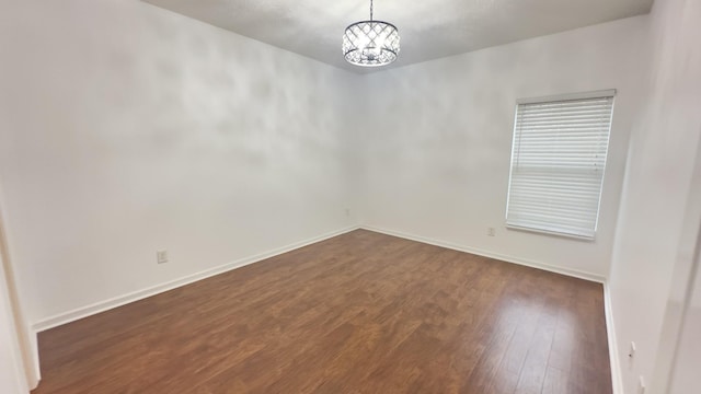 empty room with dark wood-style flooring, a chandelier, and baseboards