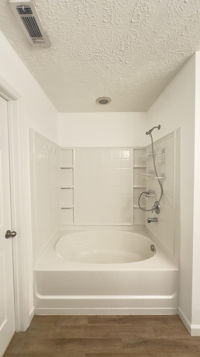 bathroom with a textured ceiling, visible vents, baseboards, bathing tub / shower combination, and wood finished floors