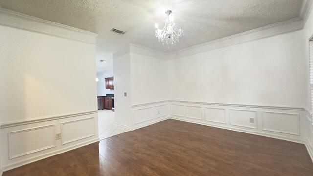 empty room with a notable chandelier, crown molding, visible vents, a decorative wall, and wood finished floors