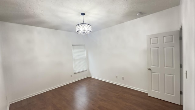 unfurnished room featuring dark wood-style floors, a textured ceiling, a notable chandelier, and baseboards