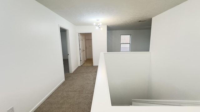 hallway with baseboards, an upstairs landing, a textured ceiling, and carpet