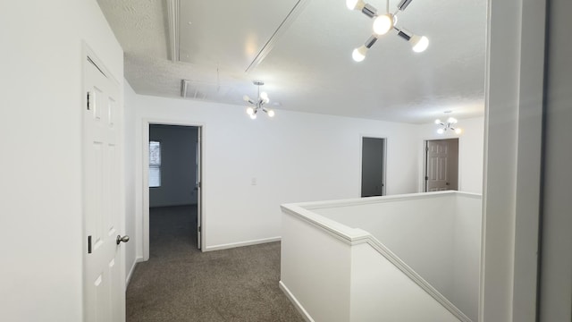 corridor with dark colored carpet, attic access, a textured ceiling, and baseboards