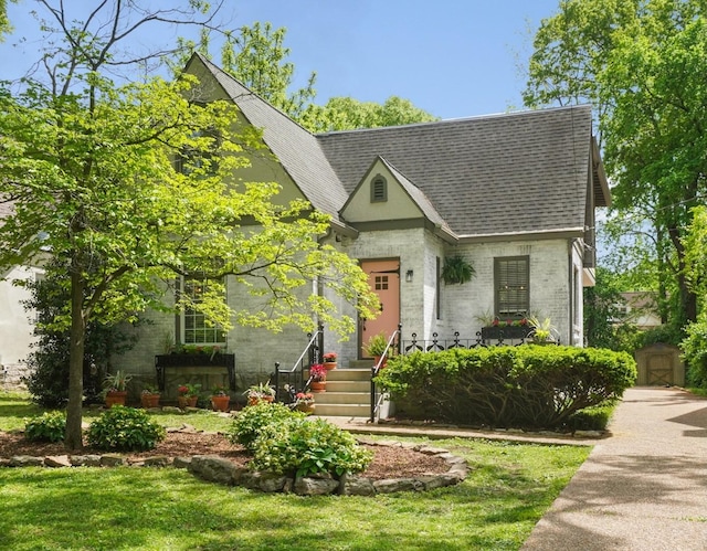 tudor home featuring brick siding and roof with shingles