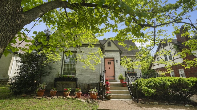 tudor home featuring a shingled roof and brick siding