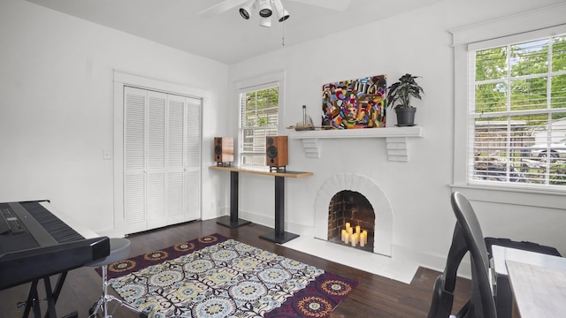 sitting room with wood finished floors, ceiling fan, baseboards, and a brick fireplace