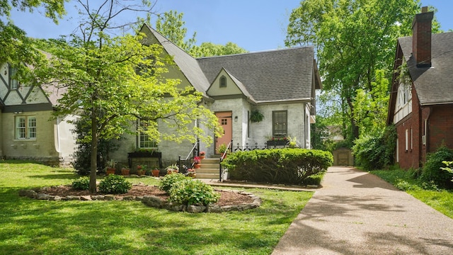 tudor home featuring a front lawn, a shingled roof, and brick siding