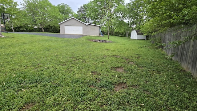 view of yard with an outbuilding, a detached garage, driveway, a shed, and fence