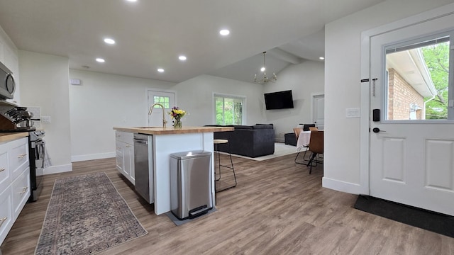 kitchen featuring white cabinets, a sink, butcher block countertops, black range, and an island with sink
