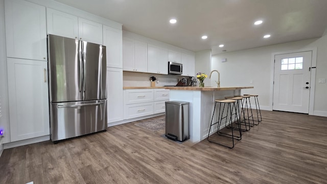 kitchen with appliances with stainless steel finishes, wood finished floors, recessed lighting, and white cabinetry
