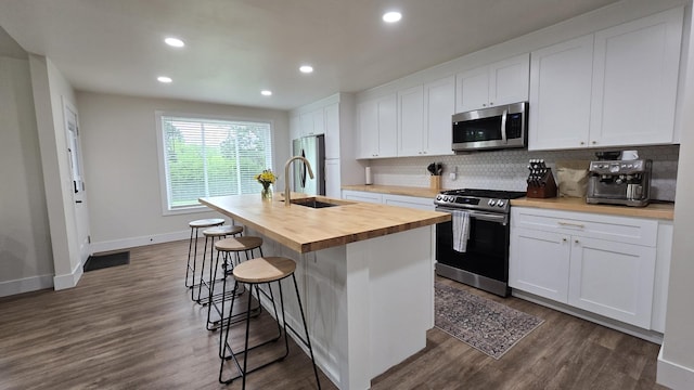 kitchen with a sink, butcher block countertops, backsplash, appliances with stainless steel finishes, and an island with sink