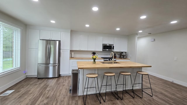 kitchen featuring stainless steel appliances, wooden counters, a sink, visible vents, and a center island with sink