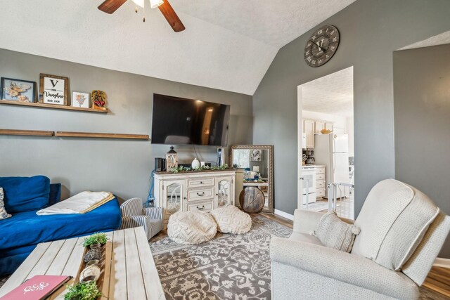living room with a ceiling fan, vaulted ceiling, wood finished floors, and baseboards