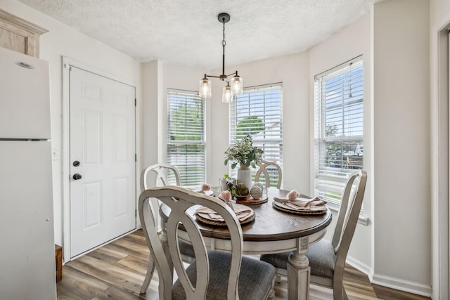 dining room featuring a textured ceiling, a notable chandelier, wood finished floors, and baseboards